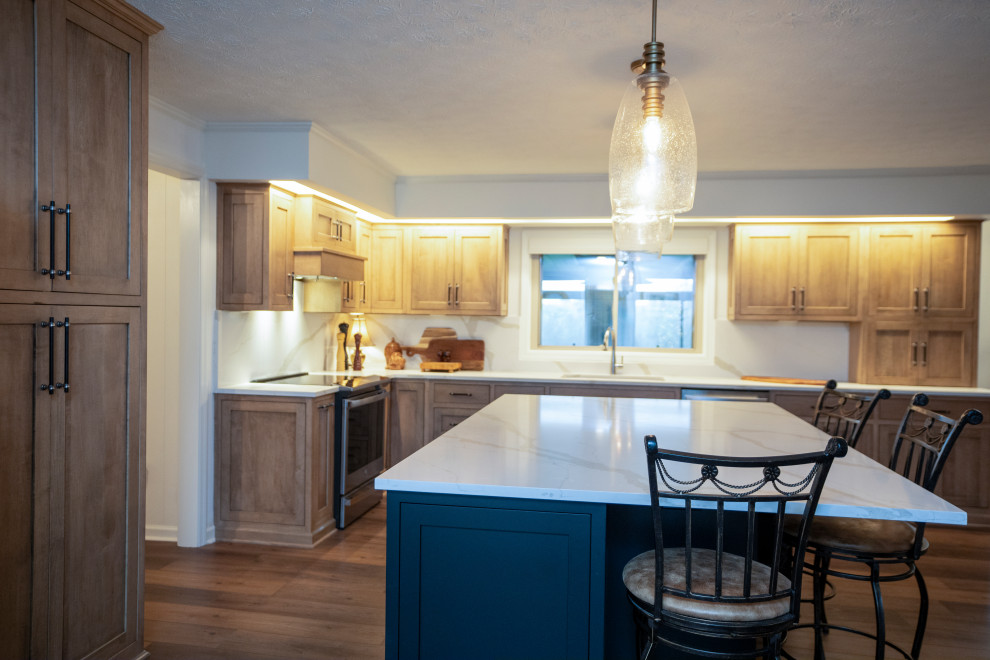 Large transitional l-shaped medium tone wood floor and brown floor eat-in kitchen photo with a single-bowl sink, shaker cabinets, medium tone wood cabinets, quartz countertops, white backsplash, quartz backsplash, stainless steel appliances, an island and white countertops