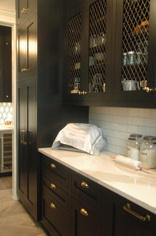 This is an example of a large traditional galley wet bar in Chicago with black cabinets, quartz benchtops, a drop-in sink, recessed-panel cabinets, white splashback, subway tile splashback, ceramic floors and grey floor.