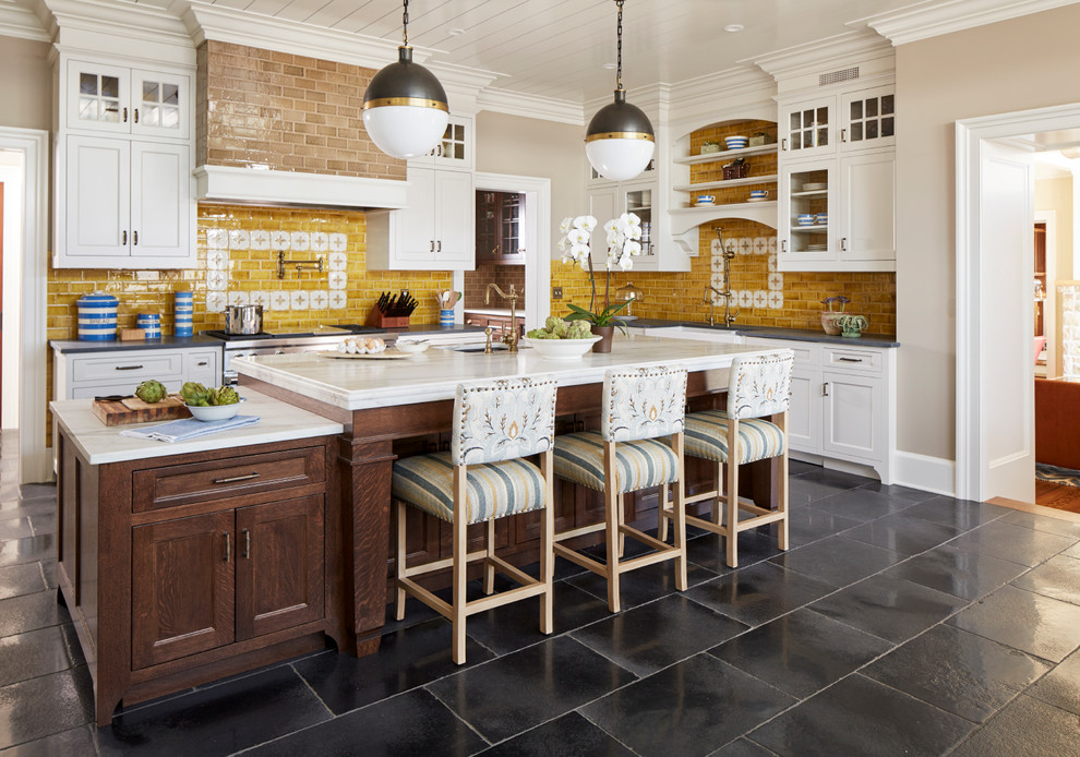 This is an example of a large country l-shaped kitchen in New York with a farmhouse sink, recessed-panel cabinets, grey cabinets, marble benchtops, yellow splashback, ceramic splashback, limestone floors, with island, stainless steel appliances and black floor.
