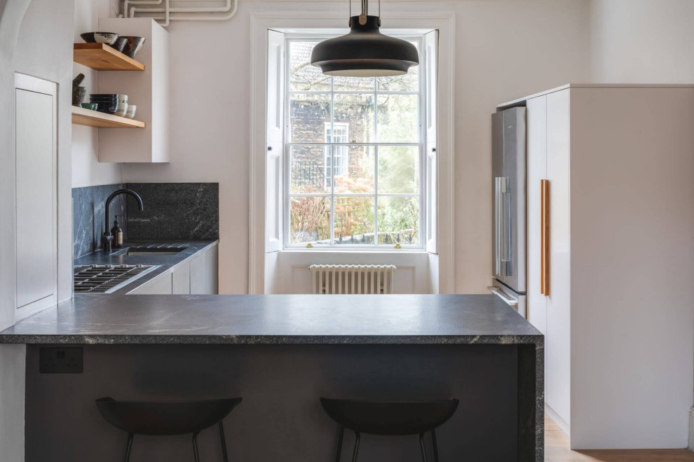 Mid-sized modern l-shaped open plan kitchen in Other with a single-bowl sink, flat-panel cabinets, black cabinets, granite benchtops, black splashback, granite splashback, black appliances and black benchtop.