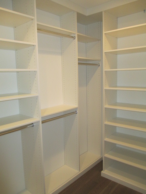 Small modern gender-neutral walk-in wardrobe in Los Angeles with medium hardwood floors, flat-panel cabinets, white cabinets and brown floor.