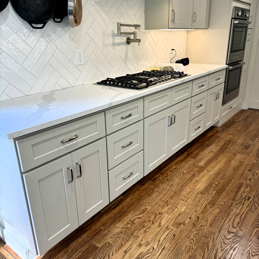 Inspiration for a mid-sized transitional u-shaped medium tone wood floor and brown floor open concept kitchen remodel in Atlanta with an undermount sink, shaker cabinets, granite countertops, white backsplash, stainless steel appliances, an island, white countertops and beige cabinets