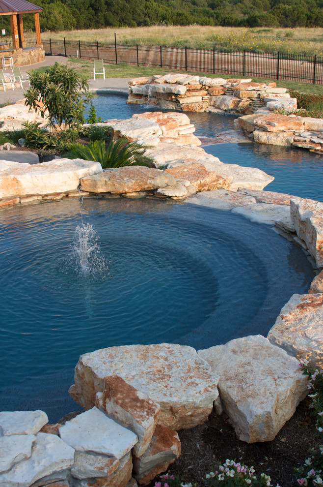This is an example of an expansive country backyard custom-shaped natural pool in Dallas with a water feature and natural stone pavers.