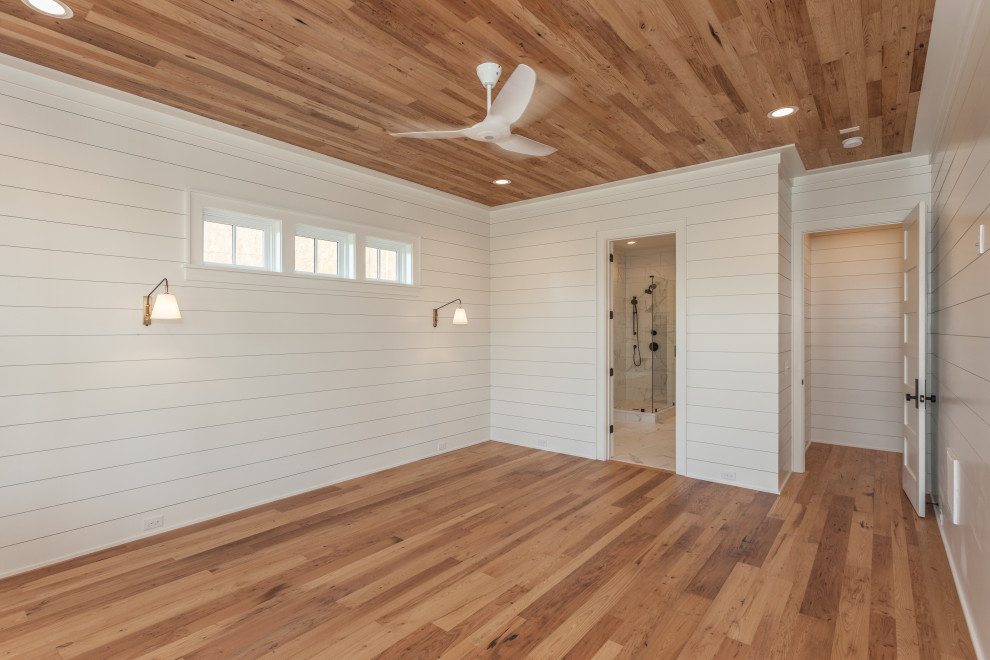 Large beach style master bedroom in Charleston with white walls, light hardwood floors, wood and planked wall panelling.