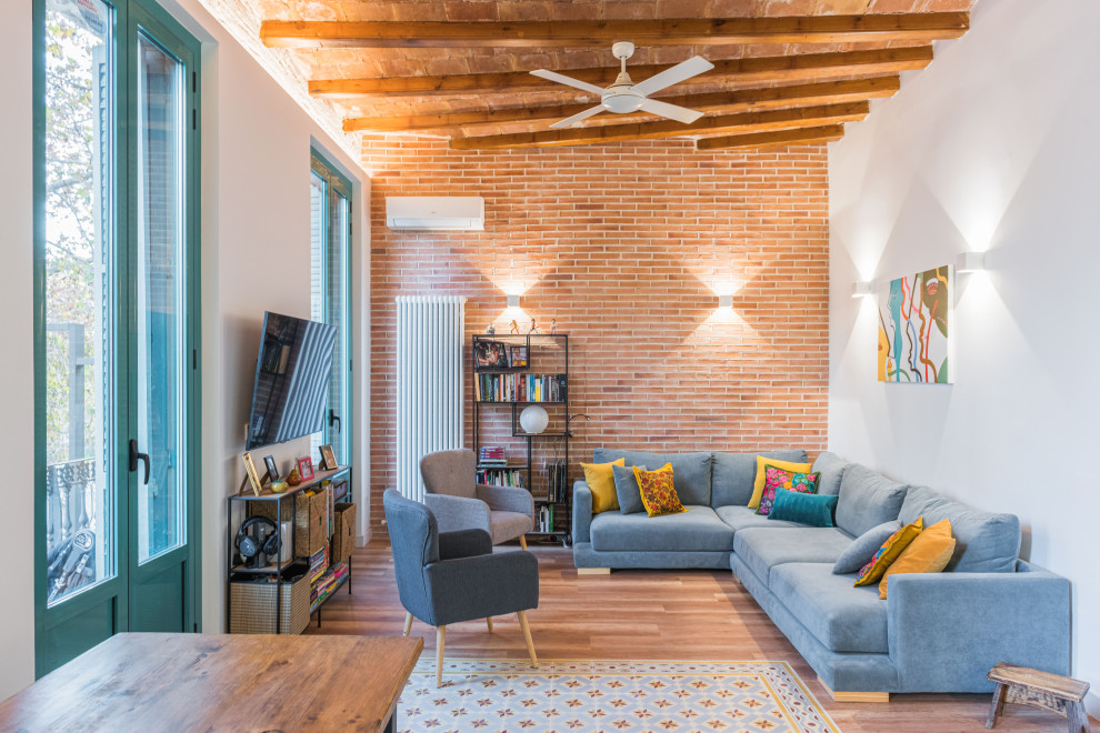 Photo of a large transitional open concept living room in Barcelona with a library, white walls, medium hardwood floors, a wall-mounted tv, beige floor, exposed beam and brick walls.