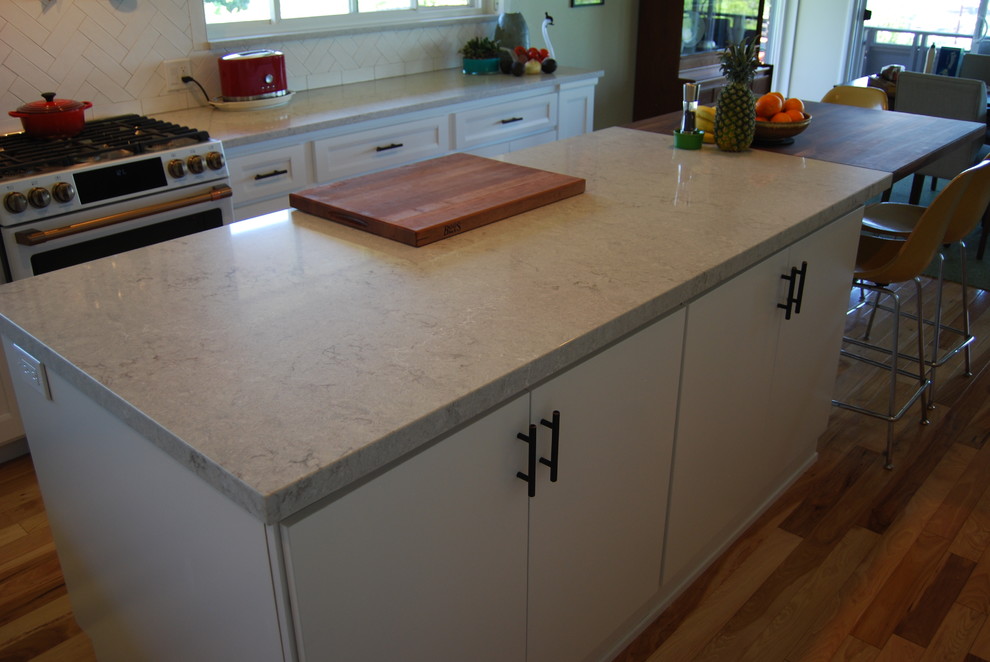 Example of a large transitional l-shaped light wood floor and brown floor eat-in kitchen design with a farmhouse sink, shaker cabinets, white cabinets, quartz countertops, white backsplash, subway tile backsplash, stainless steel appliances, an island and gray countertops