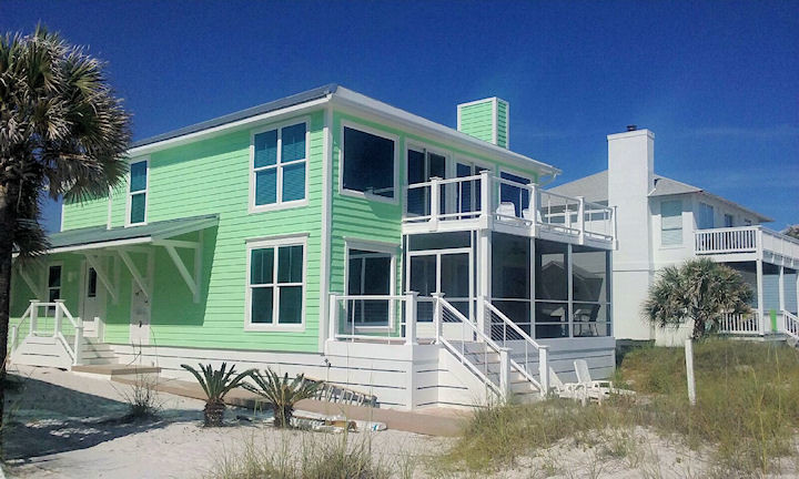 This is an example of a mid-sized beach style two-storey green house exterior in Other with vinyl siding, a flat roof and a tile roof.