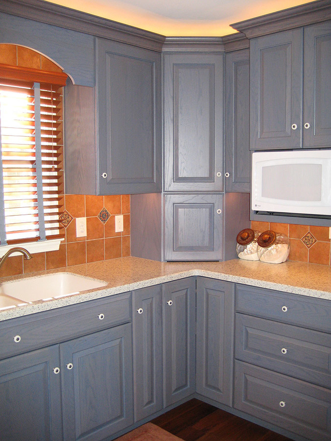 Eat-in kitchen - mid-sized transitional u-shaped eat-in kitchen idea with an integrated sink, raised-panel cabinets, blue cabinets, solid surface countertops, brown backsplash, terra-cotta backsplash and a peninsula