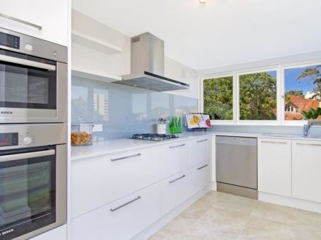 Photo of a mid-sized modern kitchen in Sydney with an undermount sink, flat-panel cabinets, white cabinets, granite benchtops, blue splashback, glass sheet splashback, stainless steel appliances and travertine floors.