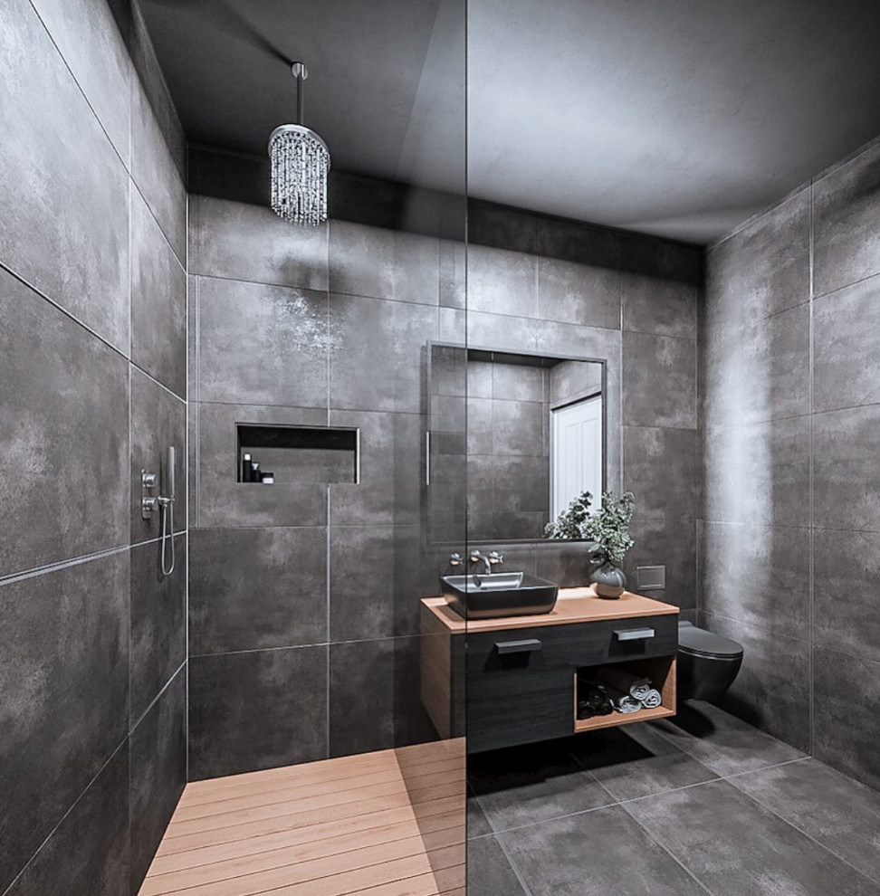 This is an example of a mid-sized contemporary master wet room bathroom in Surrey with flat-panel cabinets, black cabinets, a wall-mount toilet, gray tile, ceramic tile, grey walls, ceramic floors, a vessel sink, wood benchtops, grey floor, an open shower, brown benchtops, a single vanity and a floating vanity.