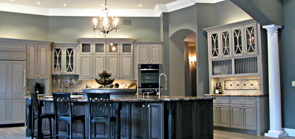 Huge transitional l-shaped porcelain tile open concept kitchen photo in Phoenix with an undermount sink, raised-panel cabinets, gray cabinets, granite countertops, gray backsplash, stone tile backsplash, stainless steel appliances and an island
