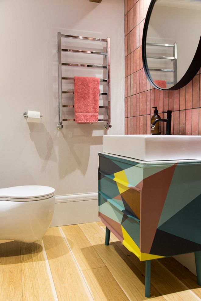 Photo of a mid-sized contemporary powder room in Kent with turquoise cabinets, a wall-mount toilet, pink tile, white walls and a freestanding vanity.