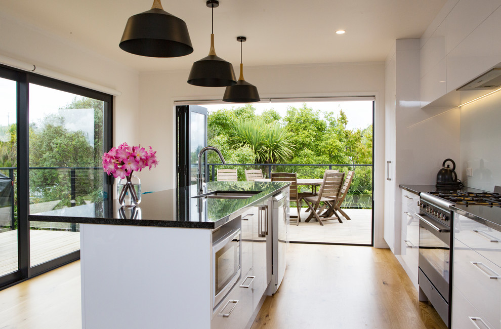 Photo of a mid-sized contemporary galley eat-in kitchen in Auckland with a double-bowl sink, white cabinets, granite benchtops, blue splashback, glass sheet splashback, black appliances, laminate floors, with island and yellow floor.