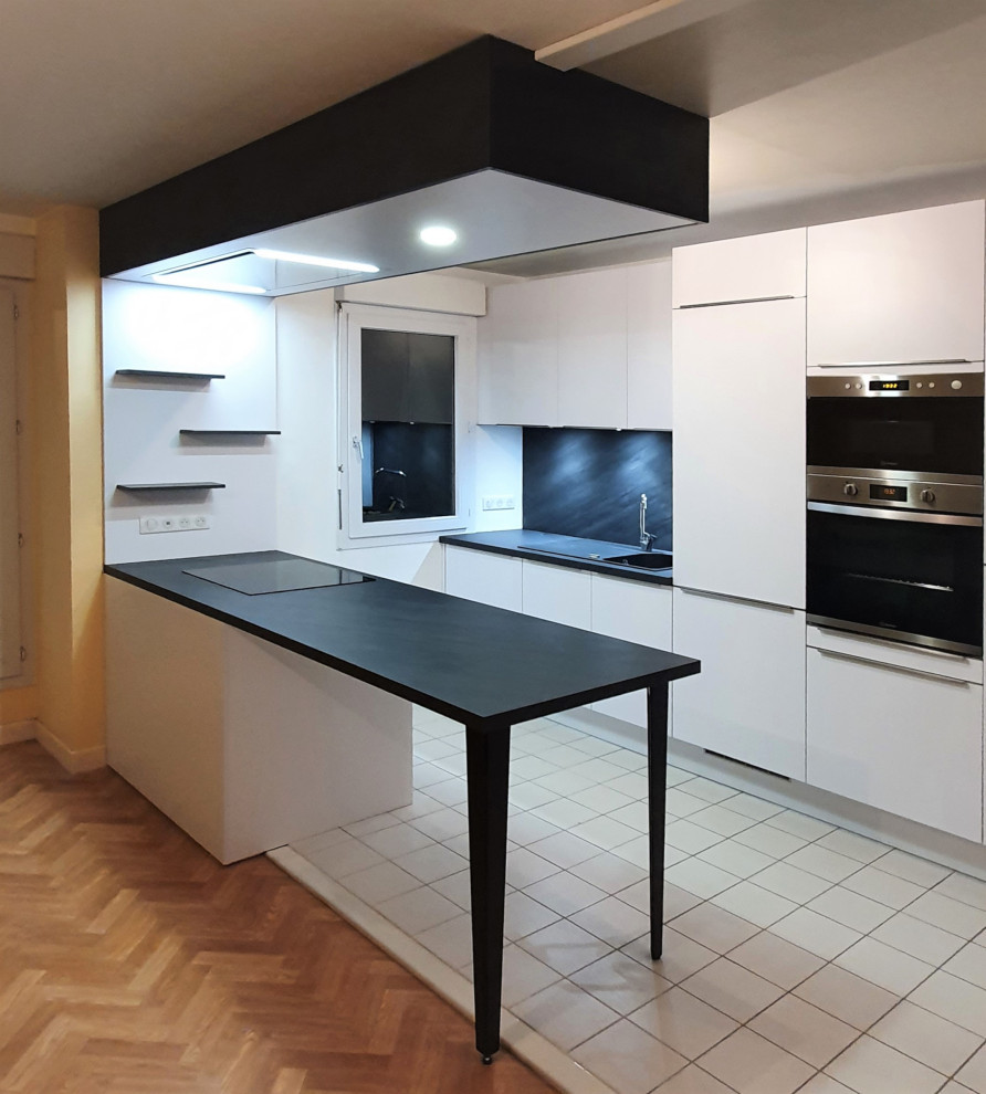 Photo of a small contemporary u-shaped open plan kitchen in Other with an undermount sink, flat-panel cabinets, stainless steel cabinets, wood benchtops, black splashback, slate splashback, panelled appliances, cement tiles, with island, white floor and black benchtop.