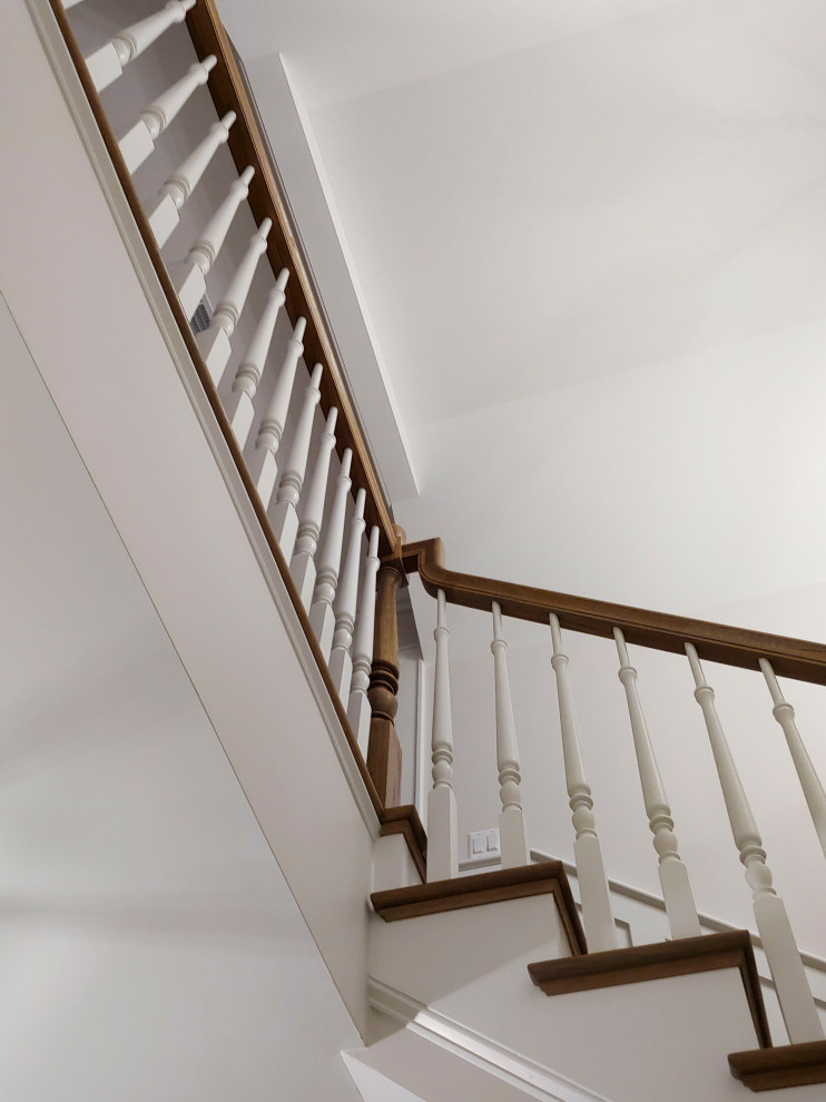 Diseño de escalera en U clásica de tamaño medio con escalones de madera, contrahuellas de madera pintada, barandilla de madera y boiserie