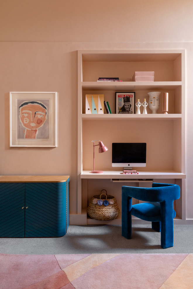 This is an example of a contemporary home office in London with pink walls, carpet, a built-in desk and grey floor.