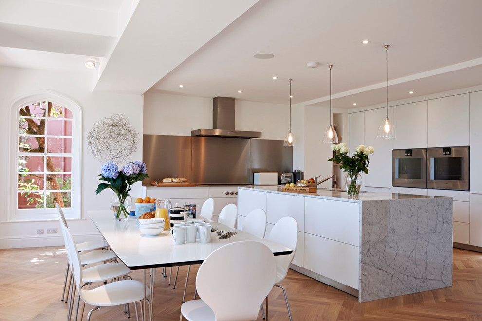 Photo of a contemporary eat-in kitchen in Gloucestershire with flat-panel cabinets, white cabinets, stainless steel appliances, medium hardwood floors and with island.