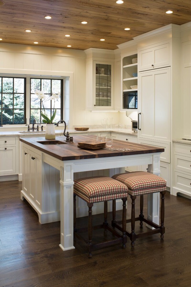Example of a large country u-shaped dark wood floor and brown floor enclosed kitchen design with an undermount sink, shaker cabinets, white cabinets, wood countertops, stainless steel appliances and an island