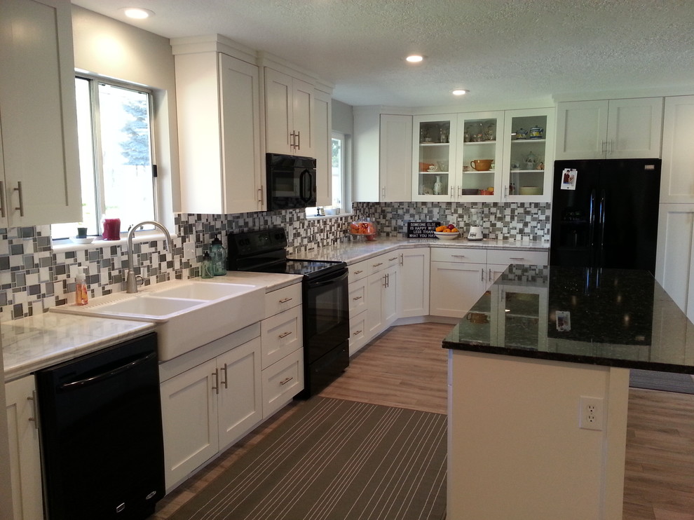Photo of a country galley eat-in kitchen in Salt Lake City with a farmhouse sink, shaker cabinets, white cabinets, granite benchtops, multi-coloured splashback, glass tile splashback, black appliances, light hardwood floors and with island.