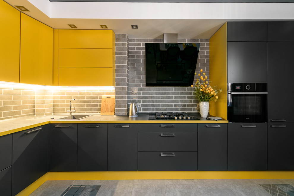 Inspiration for a mid-sized contemporary l-shaped eat-in kitchen in Other with an undermount sink, flat-panel cabinets, yellow cabinets, solid surface benchtops, black splashback, ceramic splashback, black appliances, porcelain floors, with island, grey floor and black benchtop.