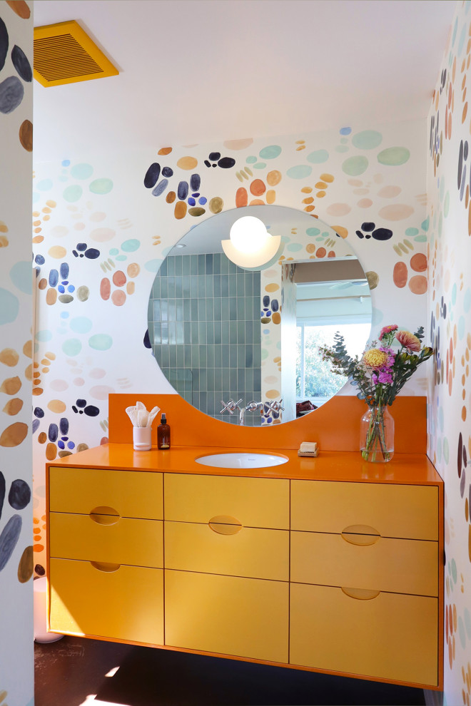 This is an example of a medium sized bohemian ensuite bathroom in Los Angeles with flat-panel cabinets, yellow cabinets, an alcove shower, a one-piece toilet, blue tiles, ceramic tiles, multi-coloured walls, concrete flooring, a submerged sink, solid surface worktops, red floors, a hinged door, orange worktops, a wall niche, a single sink, a floating vanity unit and wallpapered walls.