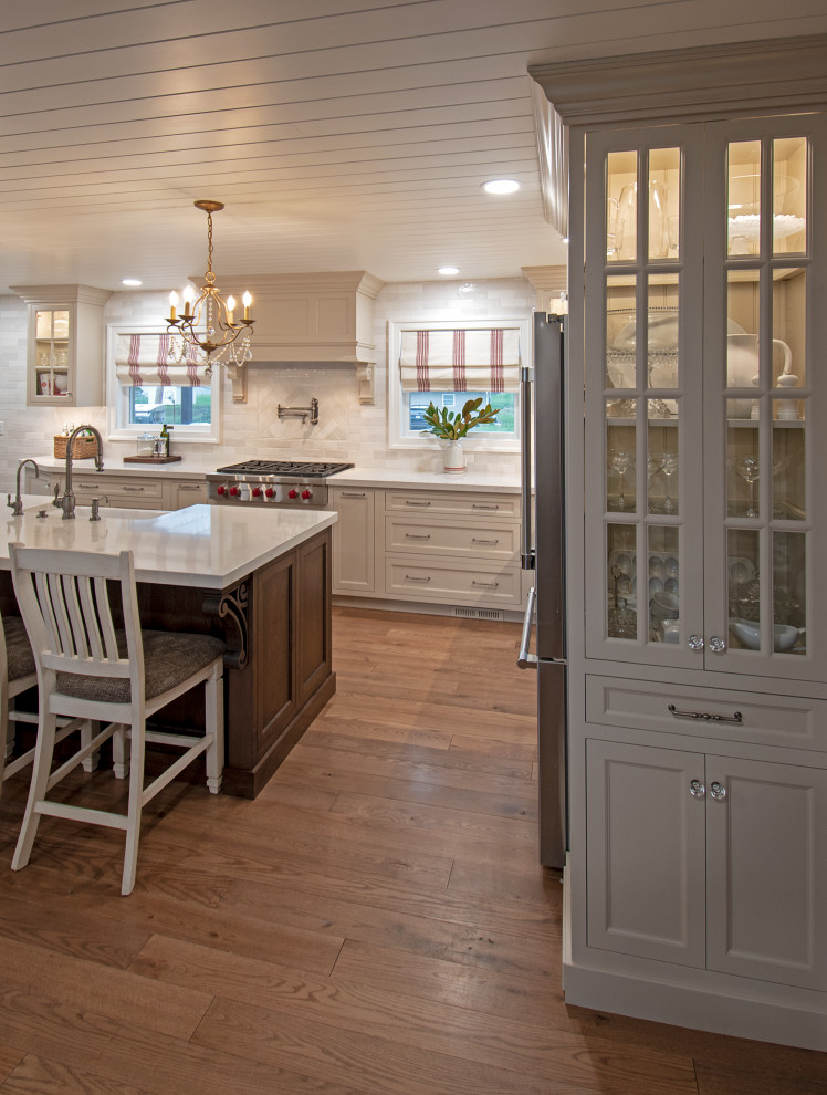 Inspiration for a transitional medium tone wood floor, brown floor and shiplap ceiling eat-in kitchen remodel with a farmhouse sink, shaker cabinets, beige cabinets, quartz countertops, white backsplash, ceramic backsplash, stainless steel appliances, an island and white countertops