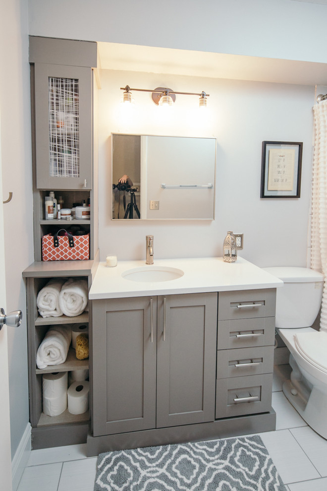 Photo of a mid-sized contemporary 3/4 bathroom in Indianapolis with shaker cabinets, grey cabinets, an alcove tub, a shower/bathtub combo, a two-piece toilet, porcelain tile, white walls, ceramic floors, an undermount sink, solid surface benchtops, white floor and a shower curtain.