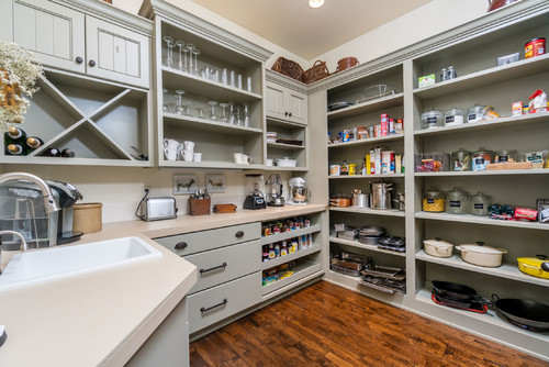 Organized butler’s pantry with sage-gray RTA cabinets, open shelves, pull-out drawers for spices, built-in wine rack, quartz counters, and a sink on warm wood floors.