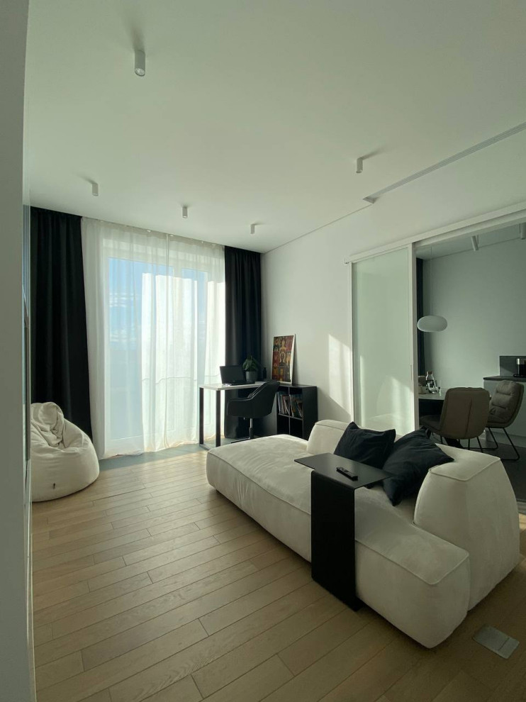 Свежая идея для дизайна: гостиная комната в белых тонах с отделкой деревом в современном стиле с белыми стенами, телевизором на стене, зоной отдыха, коричневым полом и красивыми шторами - отличное фото интерьера