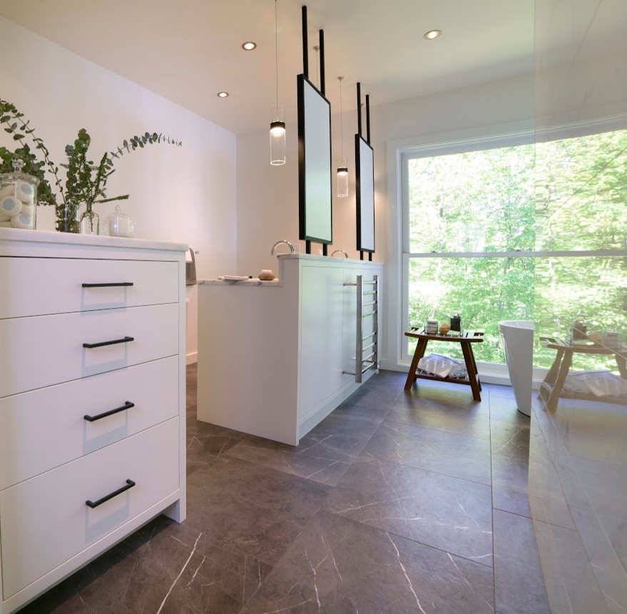 Photo of a large contemporary master bathroom in Portland Maine with flat-panel cabinets, white cabinets, a freestanding tub, a double shower, a wall-mount toilet, white tile, ceramic tile, white walls, ceramic floors, an undermount sink, marble benchtops, grey floor and a hinged shower door.
