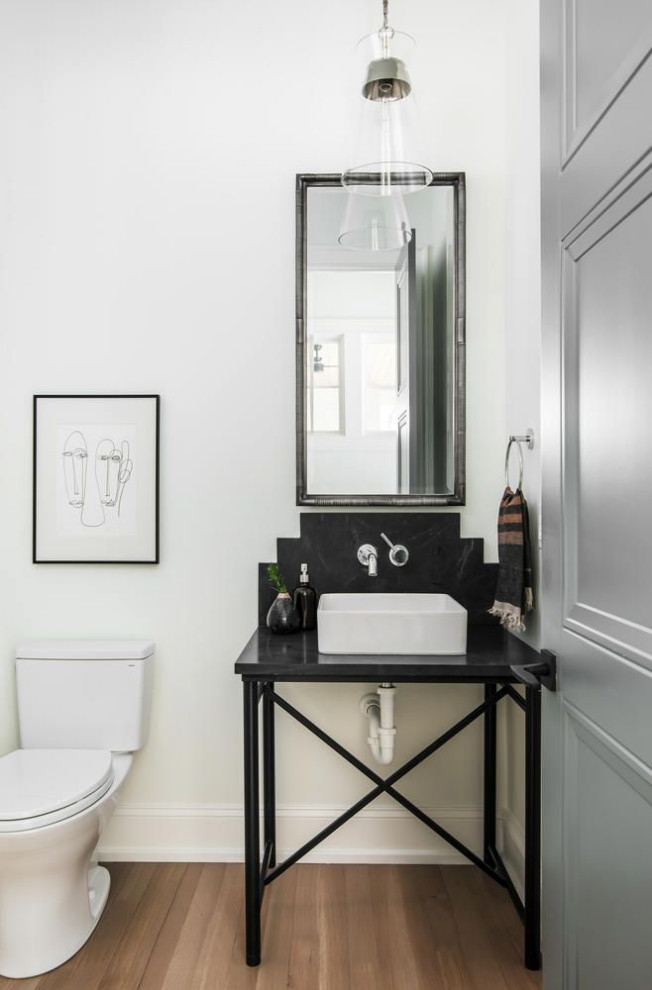 This is an example of a small transitional powder room in Nashville with open cabinets, black cabinets, a one-piece toilet, black tile, stone slab, white walls, light hardwood floors, a vessel sink, soapstone benchtops, brown floor, black benchtops and a freestanding vanity.