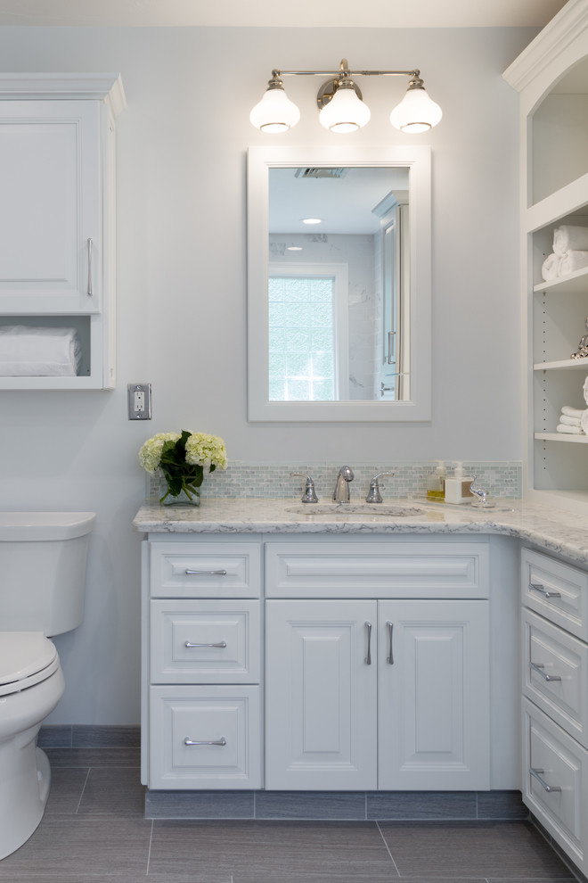 Photo of a transitional master bathroom in Providence with raised-panel cabinets, white cabinets, a drop-in tub, a corner shower, a two-piece toilet, porcelain tile, white walls, porcelain floors, an undermount sink, engineered quartz benchtops, grey floor and a hinged shower door.