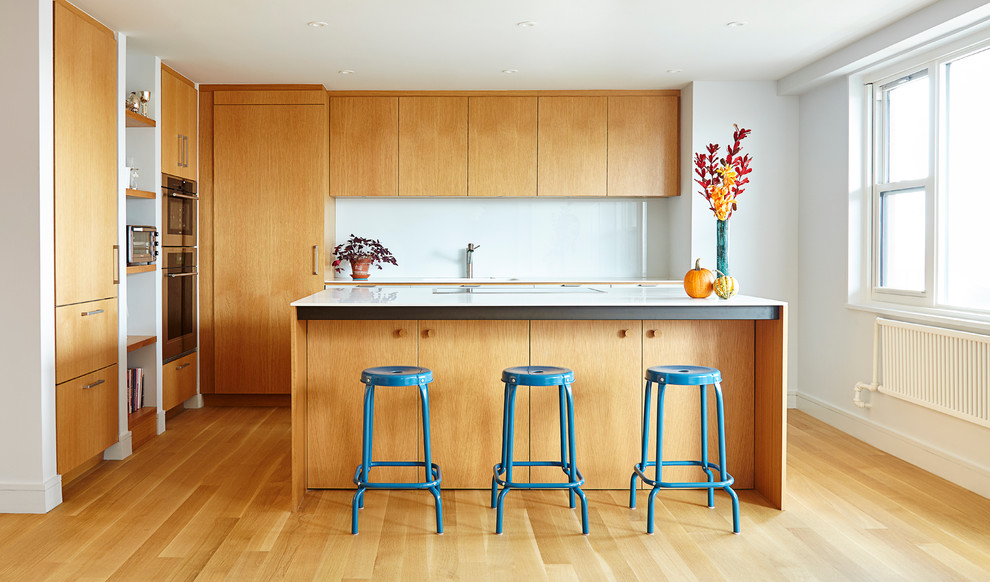Eat-in kitchen - mid-sized contemporary l-shaped light wood floor eat-in kitchen idea in New York with flat-panel cabinets, light wood cabinets, white backsplash, stainless steel appliances, an island, an undermount sink, solid surface countertops and glass sheet backsplash