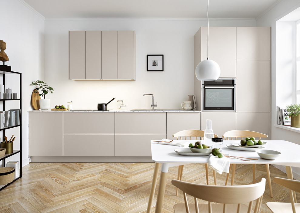 This is an example of a contemporary single-wall eat-in kitchen in Other with a drop-in sink, flat-panel cabinets, beige cabinets, white splashback, light hardwood floors and beige floor.