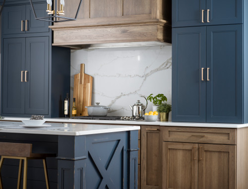 Two-tone modern kitchen with navy blue and natural wood cabinets, brass handles, marble backsplash, and a white quartz island — Kitchen Cabinet Mississauga.