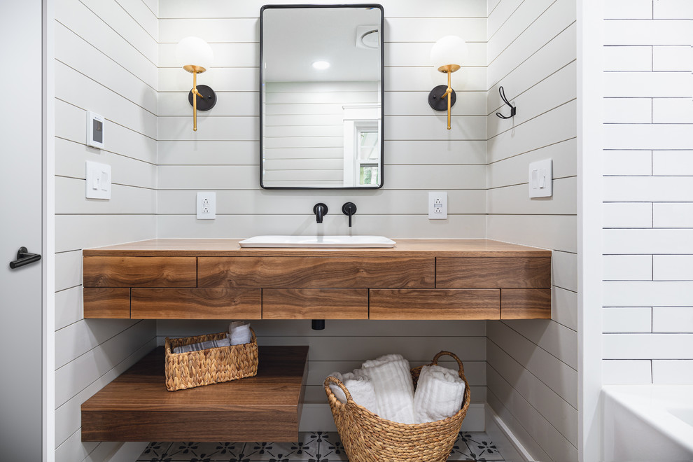 Design ideas for a mid-sized country bathroom in Other with furniture-like cabinets, medium wood cabinets, an alcove tub, a shower/bathtub combo, a two-piece toilet, white tile, ceramic tile, grey walls, porcelain floors, wood benchtops, grey floor, a shower curtain, a vessel sink, a floating vanity and planked wall panelling.