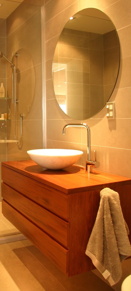 Inspiration for a large eclectic bathroom in Auckland with raised-panel cabinets, orange cabinets, a one-piece toilet, beige tile, porcelain tile, beige walls, ceramic floors, a vessel sink, wood benchtops and beige floor.
