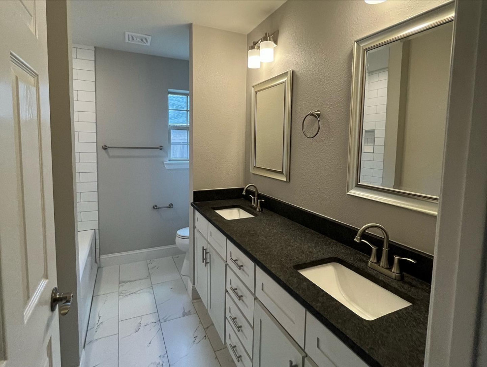 Mid-sized transitional white tile and subway tile porcelain tile, white floor and double-sink drop-in bathtub photo in Dallas with shaker cabinets, white cabinets, a two-piece toilet, gray walls, an undermount sink, quartz countertops, black countertops, a niche and a built-in vanity