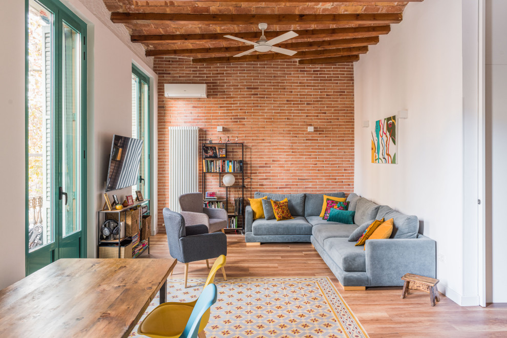 Large contemporary open concept living room in Barcelona with white walls, medium hardwood floors, a wall-mounted tv, exposed beam, brick walls and brown floor.