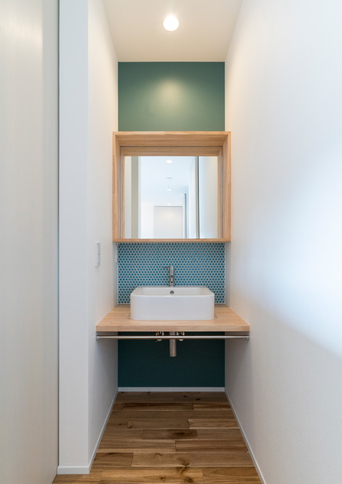 Design ideas for a small scandinavian powder room in Kyoto with open cabinets, light wood cabinets, green tile, mosaic tile, white walls, medium hardwood floors, a vessel sink, wood benchtops, beige floor, beige benchtops, a floating vanity, wallpaper and wallpaper.