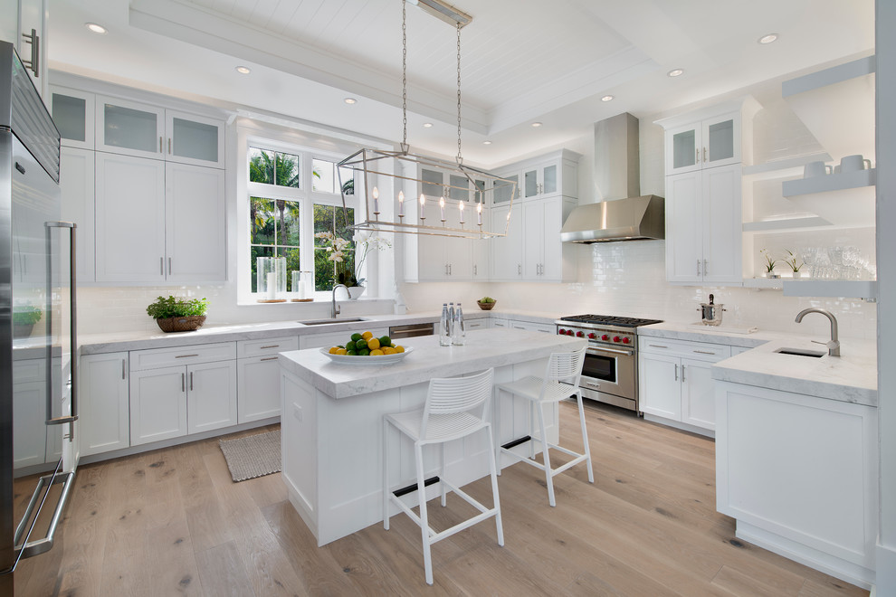 Transitional u-shaped light wood floor kitchen photo with an undermount sink, shaker cabinets, white cabinets, white backsplash, subway tile backsplash, stainless steel appliances and an island
