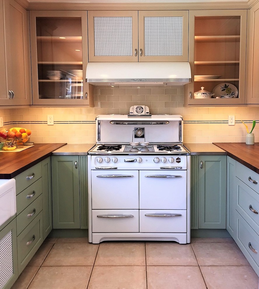 Design ideas for a mid-sized country u-shaped separate kitchen in Orange County with a farmhouse sink, shaker cabinets, green cabinets, wood benchtops, ceramic splashback, white appliances, porcelain floors and no island.