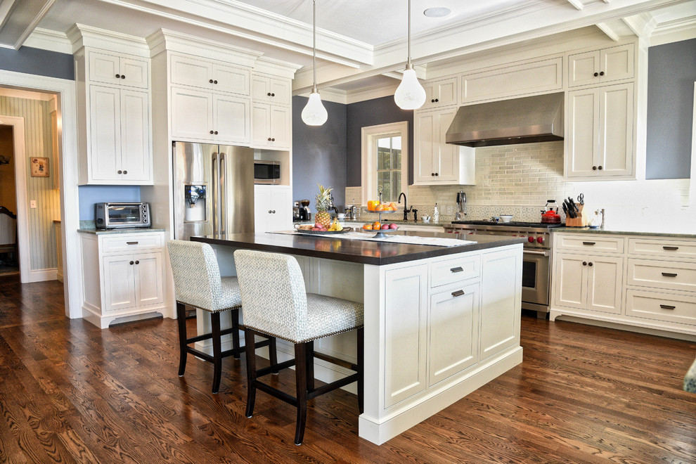 This is an example of a traditional u-shaped kitchen in Portland Maine with shaker cabinets, white cabinets, white splashback, stainless steel appliances, dark hardwood floors and with island.