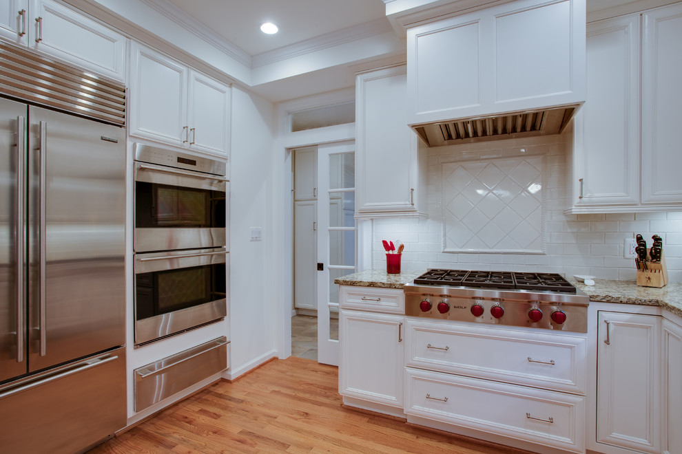 Mid-sized traditional eat-in kitchen in DC Metro with white cabinets, granite benchtops, stainless steel appliances and light hardwood floors.