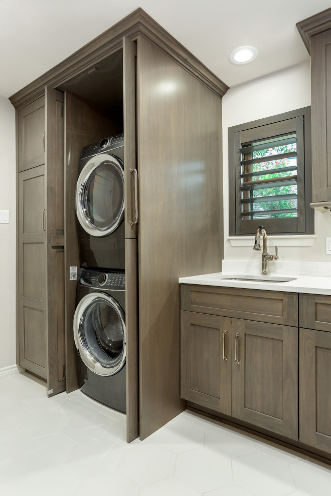 Inspiration for a large transitional single-wall utility room in Dallas with an undermount sink, recessed-panel cabinets, grey cabinets, quartz benchtops, white splashback, engineered quartz splashback, beige walls, dark hardwood floors, a stacked washer and dryer, brown floor and white benchtop.