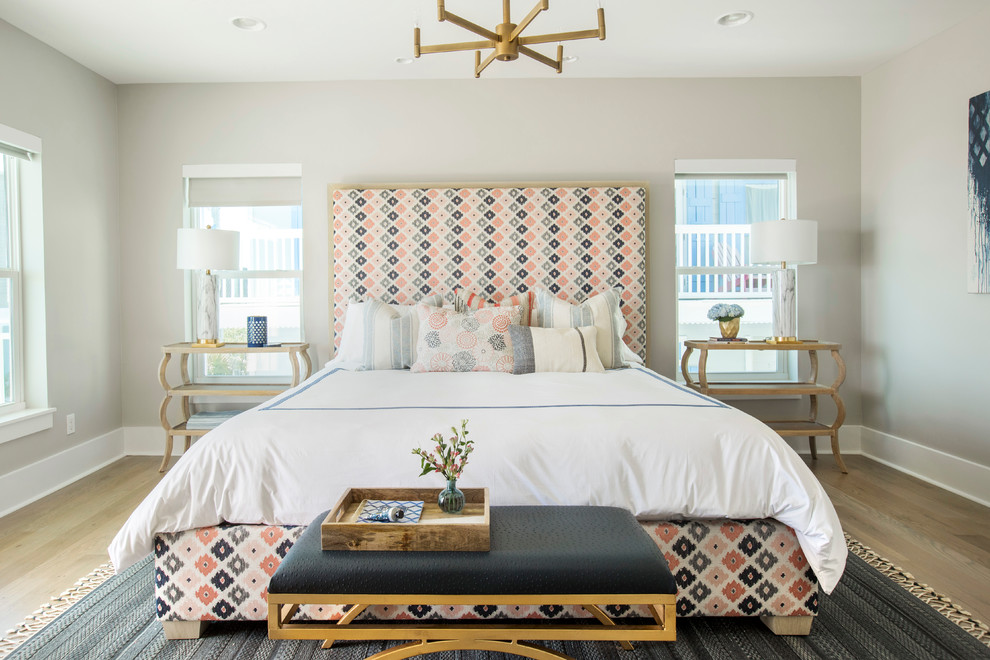 This is an example of a large beach style bedroom in Miami with beige walls and light hardwood floors.