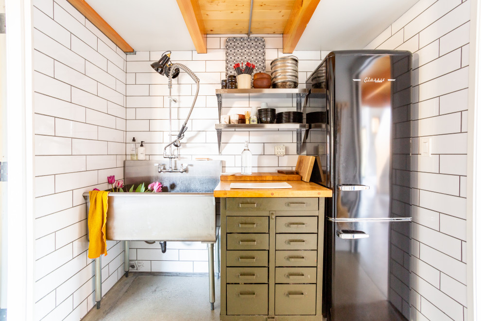 Inspiration för ett avskilt, litet industriellt brun linjärt brunt kök, med en enkel diskho, träbänkskiva, vitt stänkskydd, stänkskydd i keramik, svarta vitvaror, betonggolv och grått golv