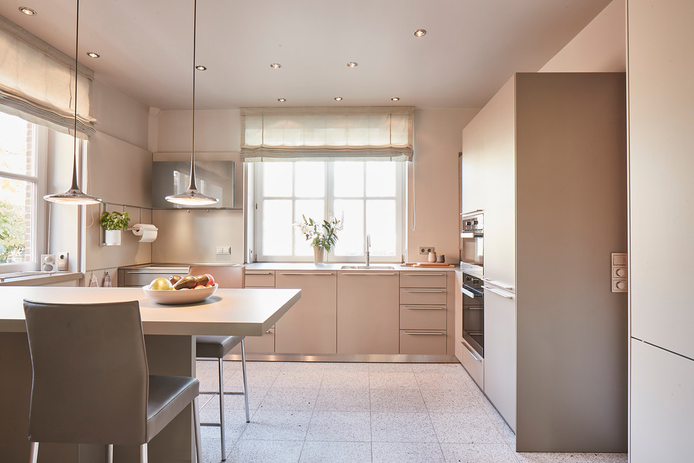 Large contemporary l-shaped eat-in kitchen in Hamburg with flat-panel cabinets, grey cabinets, beige splashback, stainless steel appliances, terrazzo floors, a peninsula, beige floor, beige benchtop and an undermount sink.