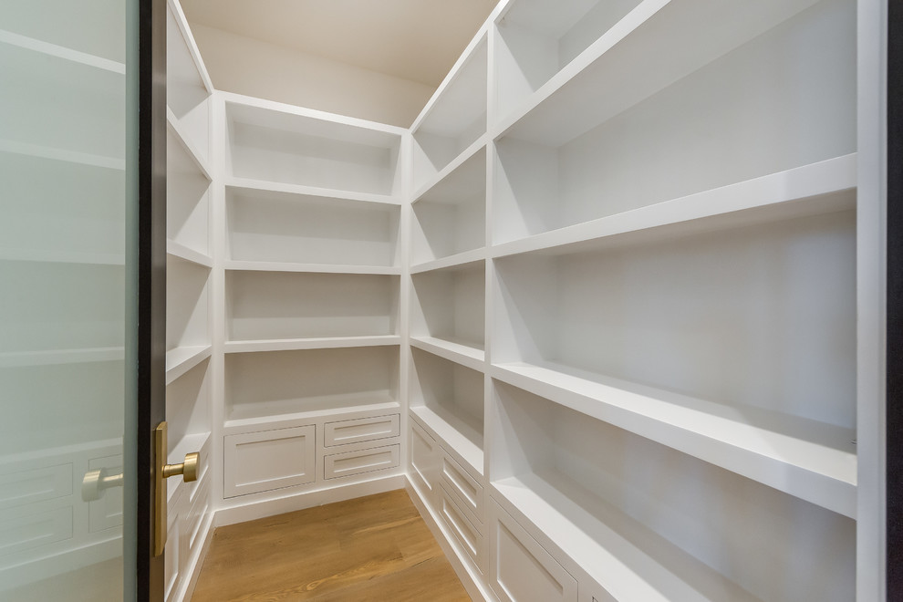 Inspiration for a small transitional gender-neutral walk-in wardrobe in Los Angeles with white cabinets, light hardwood floors, brown floor and recessed-panel cabinets.