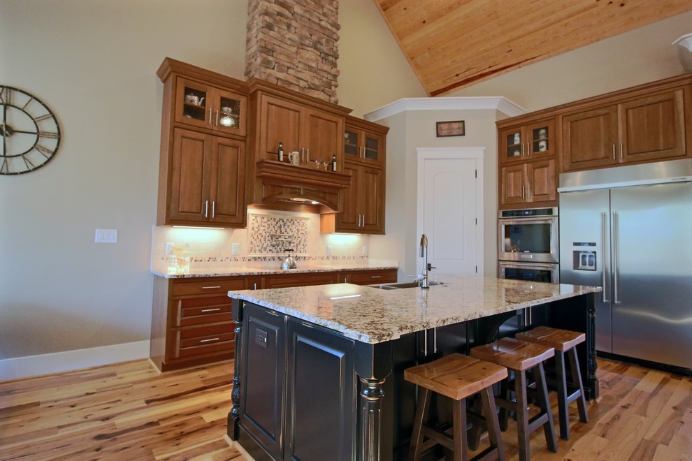 Inspiration for a mid-sized transitional l-shaped light wood floor and beige floor kitchen pantry remodel in Raleigh with a farmhouse sink, raised-panel cabinets, medium tone wood cabinets, granite countertops, multicolored backsplash, glass tile backsplash, stainless steel appliances, an island and brown countertops